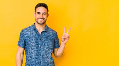 Sarı fırında izole edilmiş genç beyaz adam zafer işareti gösteriyor ve gülümsüyor..