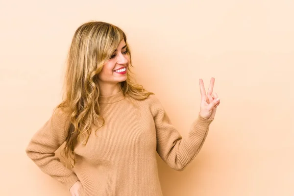 Young blonde caucasian woman joyful and carefree showing a peace symbol with fingers.