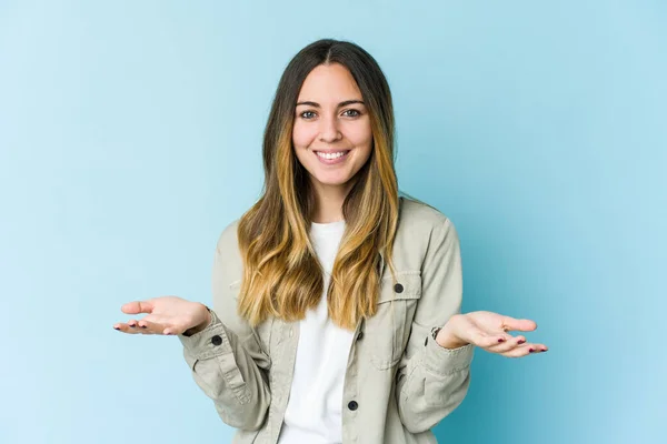 Young Caucasian Woman Isolated Blue Background Makes Scale Arms Feels — Stock Photo, Image