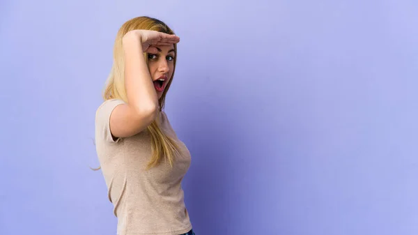 Молодая Блондинка Изолированы Фиолетовом Фоне Глядя Далеко Держа Руку Лбу — стоковое фото