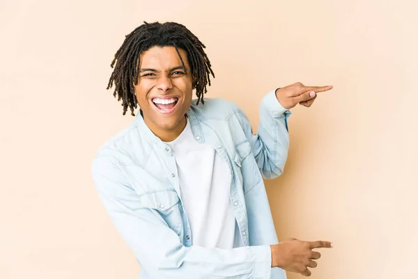 Young african american rasta man excited pointing with forefingers away.