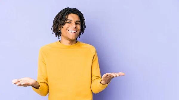 Young black man wearing rasta hairstyle makes scale with arms, feels happy and confident.