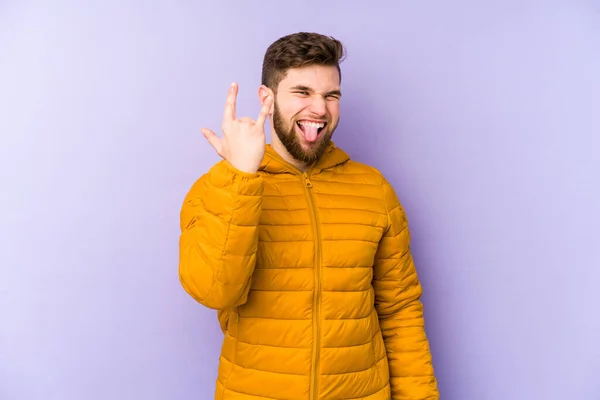 Young man isolated on purple background showing rock gesture with fingers
