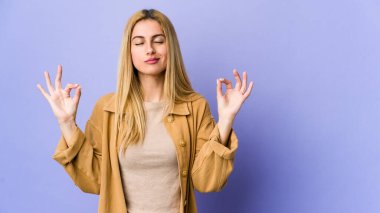 Mor arka planda izole edilmiş genç sarışın kadın yoğun bir günün ardından rahatlıyor, yoga yapıyor..