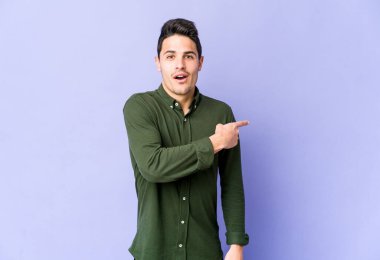 Mor arka planda izole edilmiş genç beyaz adam yan tarafı işaret ediyor.