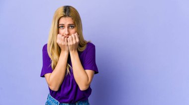 Young blonde woman isolated on purple background biting fingernails, nervous and very anxious. clipart