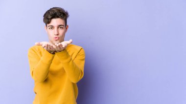 Mor arka planda izole edilmiş genç beyaz adam dudakları katlıyor ve hava öpücüğü göndermek için avuç içleri tutuyor..