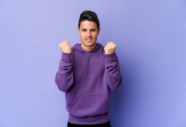 Mor arka planda izole edilmiş genç beyaz adam yumruğunu kameraya gösteriyor, agresif yüz ifadesi var..