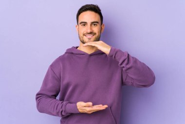 Mor arka planda izole genç beyaz adam iki eliyle bir şey tutuyor, ürün sunumu..