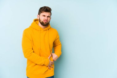 Mavi arka planda karaciğer ağrısı çeken, karnı ağrıyan genç beyaz bir adam..