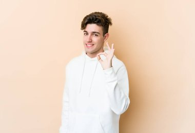 Beyazlı genç bir adam bej arka planda izole edilmiş bir şekilde göz açıp kapayıncaya kadar elinde iyi bir el hareketi tutuyor..