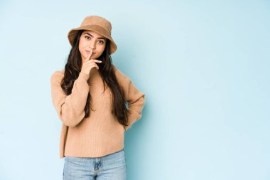 Mavi arka planda izole edilmiş bir şapka takan genç Hintli kadın düşünüyor, düşünüyor, düşünüyor, hayal kuruyor..