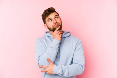 Pembe arka planda izole edilmiş genç beyaz adam şüpheli ve şüpheci bir ifadeyle yana bakıyor..