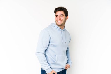 Beyaz arka planda soyutlanmış genç bir adam gülümseyen, neşeli ve keyifli bir kenara bakıyor..