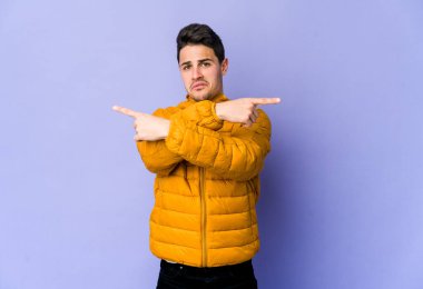 Mor arka plan noktalarında izole genç beyaz adam, iki seçenek arasında seçim yapmaya çalışıyor.