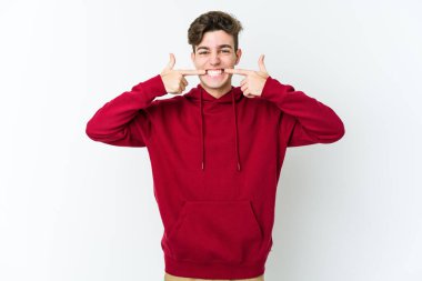 Beyaz arka planda izole edilmiş genç beyaz adam gülümsüyor, parmaklarını ağıza doğrultuyor..
