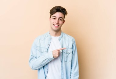 Beyaz tenli genç adam bej arka planda izole edilmiş gülümsüyor ve boş alanda bir şeyler gösteriyor..