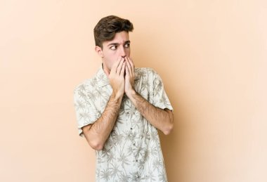 Beyazlı genç bir adam bej arka planda izole edilmiş. Düşünceli bir şekilde bir fotokopi odasına bakıyor. Ağzını eliyle kapatıyor..