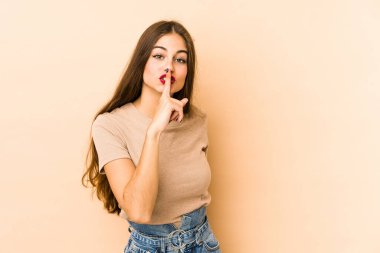 Beyazlı genç bir kadın bej arka planda izole edilmiş bir şekilde ya sır saklıyor ya da sessizlik istiyor..