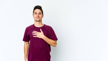 Beyaz arka planda izole edilmiş genç beyaz adam yemin ediyor, elini göğsüne koyuyor..