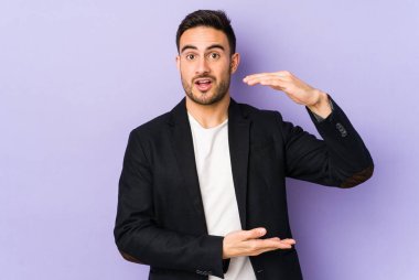 Mor arka planda izole genç beyaz adam iki eliyle bir şey tutuyor, ürün sunumu..
