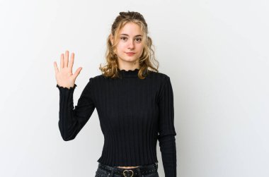 Beyaz arka plandaki genç beyaz kadın gülümseyerek beş numarayı parmaklarıyla gösteriyor..