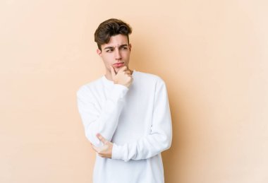Beyazlı genç adam bej arka planda izole edilmiş şüpheli ve şüpheci bir ifadeyle yana bakıyor..