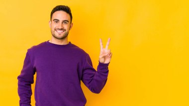 Kafkasyalı genç adam sarı fırında izole edilmiş neşeli ve kaygısız parmaklarıyla barış sembolü gösteriyor..