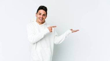 Beyaz arka planda izole edilmiş genç beyaz bir adam, palmiye üzerinde bir fotokopi alanı tutarken heyecanlı..