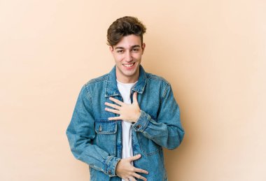 Beyazların arka planında izole edilmiş genç beyaz adam mutlu bir şekilde gülüyor ve ellerini karnının üstünde tutarak eğleniyor..