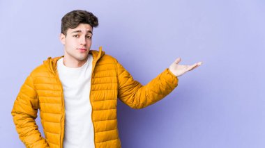 Mor arka planda izole edilmiş genç beyaz adam sorgulama sırasında omuz silkiyor ve şüphe duyuyor..