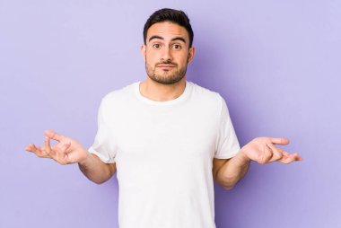 Mor arka planda izole edilmiş genç beyaz adam sorgulama sırasında omuz silkiyor ve şüphe duyuyor..