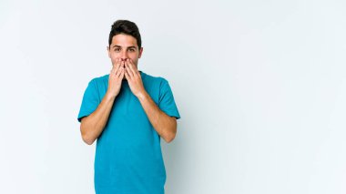 Beyaz arka planda izole edilmiş genç beyaz adam şok olmuş, ağzı ellerle kaplanmış, yeni bir şey keşfetmeye hevesli..