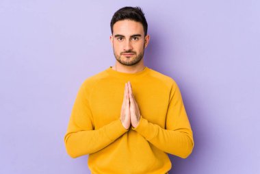 Mor arka planda izole edilmiş genç beyaz adam dua ediyor, bağlılık gösteriyor, dindar biri ilahi ilham arıyor..