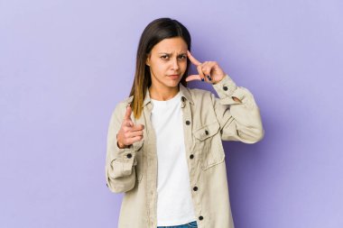 Mor arka planda izole edilmiş genç bir kadın şakağı parmağıyla işaret ediyor, düşünüyor ve bir göreve odaklanıyor..
