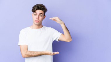 Mor arka planda izole genç beyaz adam iki eliyle bir şey tutuyor, ürün sunumu..