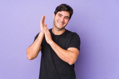 Mor arka planda izole olmuş genç bir adam enerjik ve rahat hissediyor, ellerini ovuşturuyor, kendinden emin..