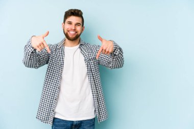 Kafkasyalı genç adam mavi arka planda izole edildi. Parmakları aşağıda, olumlu bir his var..