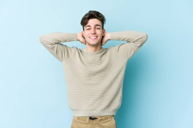 Kafkasyalı genç adam mavi arka planda izole edilmiş. Kendine güveniyor, elleri başının arkasında..