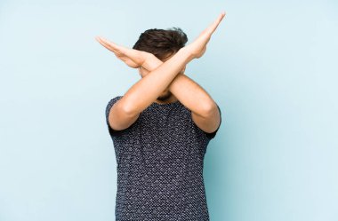 Genç Arap bir adam mavi bir arka planda izole edilmiş iki kolu çapraz tutuyor, inkar kavramı.