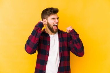 Sarı arka planda izole edilmiş genç beyaz adam zaferden sonra yumruğunu kaldırıyor, kazanan konsept..