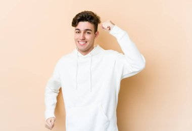 Beyaz tenli genç adam bej arka planda izole edilmiş tasasız ve heyecanlı tezahüratlar yapıyor. Zafer konsepti.