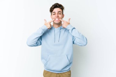 Beyaz arka planda izole edilmiş genç beyaz adam gülümsüyor, parmaklarını ağıza doğrultuyor..
