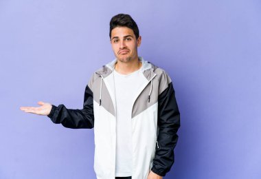 Mor arka planda izole edilmiş genç beyaz bir adam bir avuç içinde fotokopi alanı ve belinde bir el daha gösteriyor..