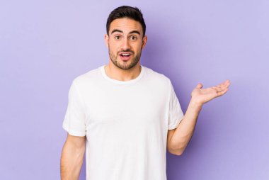 Mor arka planda izole edilmiş genç beyaz adam, avuç içi fotokopi alanını elinde tutmaktan etkilenmiş..