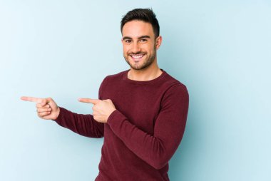 Kafkasyalı genç adam mavi arka planda izole edilmiş. İşaret parmağıyla işaret ettiği için heyecanlı..