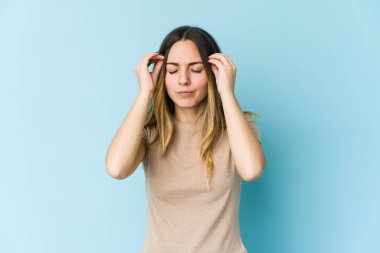 Mavi arka planda izole edilmiş genç beyaz kadın şakaklara dokunuyor ve baş ağrısı çekiyor..