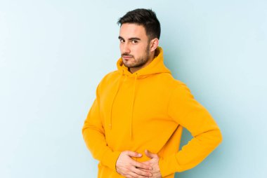 Mavi arka planda karaciğer ağrısı çeken, karnı ağrıyan genç beyaz bir adam..