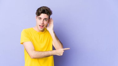 Mor arka planda izole edilmiş genç beyaz bir adam bir dedikoduyu dinlemeye çalışıyor..