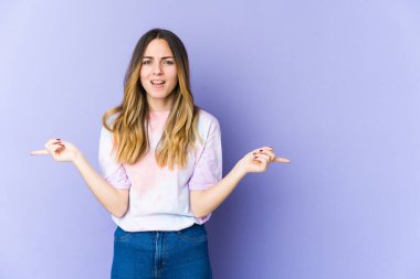 Mor arka planda izole edilmiş genç beyaz kadın farklı kopya alanlarını gösteriyor, birini seçiyor, parmaklarıyla gösteriyor.